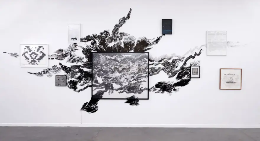 Œuvres d'Abdelkader Benchamma : une explosion d'encre noire sur mur blanc, encadrée par des dessins et peintures.
