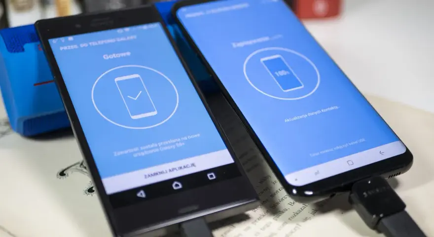 Dwa telefony połączone kablem USB. Jeden pokazuje "Gotowe", drugi "100%". To pokazuje, jak przenieść dane z telefonu na telefon.