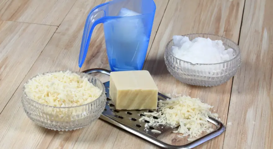Ingrédients pour une lessive maison : savon râpé, cristaux de soude et un bloc de savon sur une râpe.