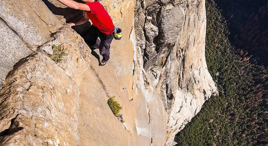Ein Mann klettert free solo eine steile Felswand empor, mit einem tiefen Abgrund unter ihm.