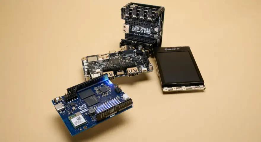 An Arduino Uno, a Bela GEN MULTI, and a Fruit Jam RP2350 board are arranged on a beige surface, showcasing some of the best microcontroller options for makers.