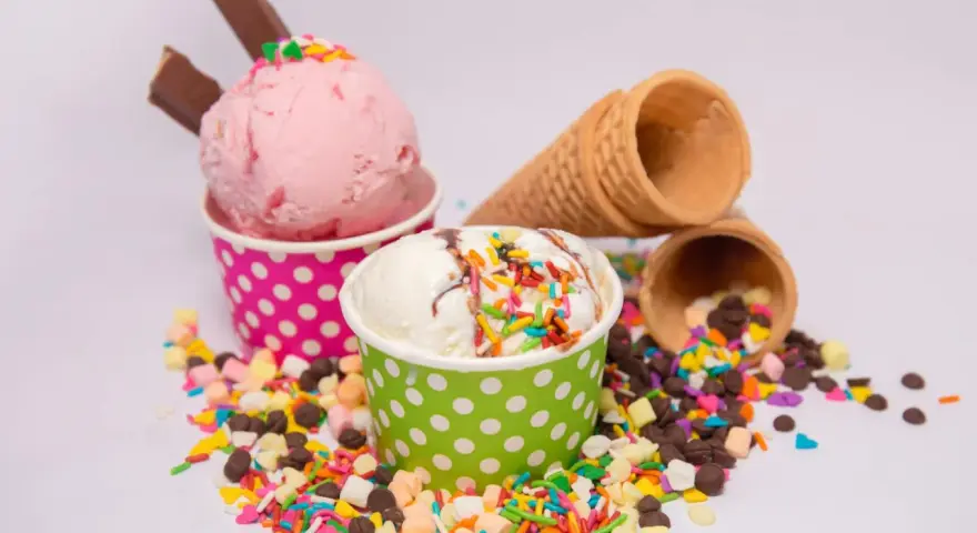 Zwei Becher mit Eiscreme, einer rosa, der andere weiß, bestreut mit bunten Streuseln und Schokostückchen. So sieht leckeres Gelato aus!