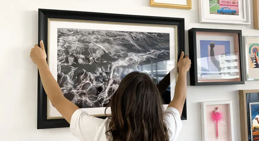 Une femme ajuste un grand cadre noir avec une photo d'eau en noir et blanc. Elle est en train de fabriquer un cadre pour sa maison.