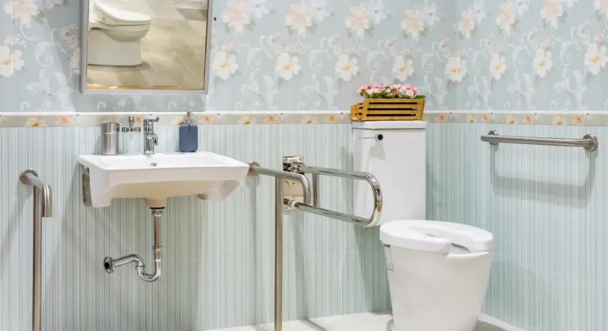 Salle de bain senior : lavabo suspendu, WC avec barre d'appui rabattable et barre d'appui murale pour plus de sécurité.