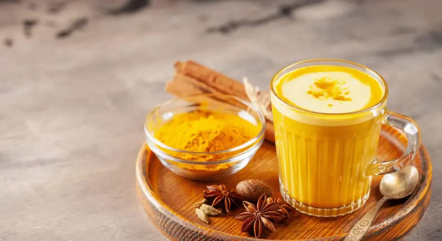 Ein Glas goldene Milch mit Kurkumapulver, Zimtstangen und Sternanis. Perfekt für ein wärmendes goldene milch rezept.