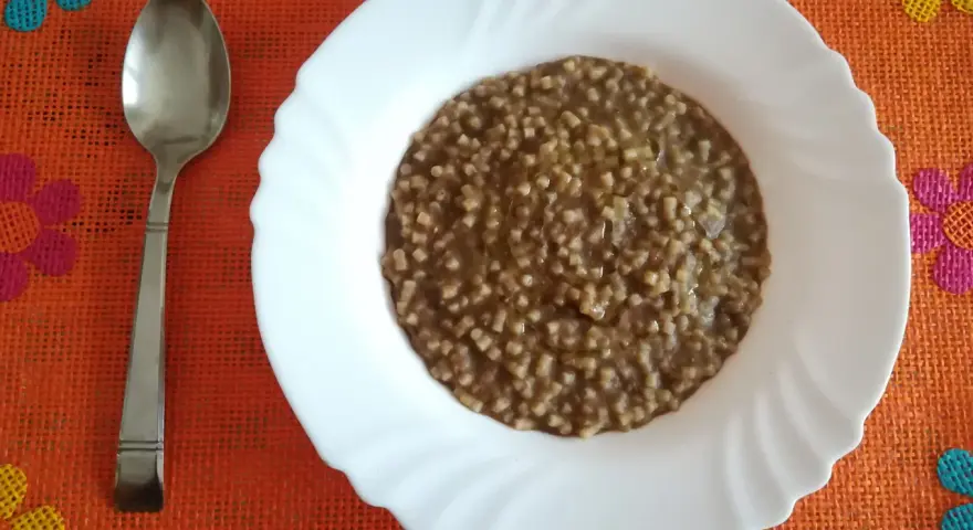 Piatto di pasta e lenticchie fumante, pronto per essere gustato. Un cucchiaio d'argento attende accanto.