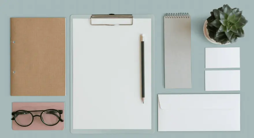 Un exemple de book artistique : un carnet brun, des lunettes, un presse-papiers avec un crayon, un carnet gris, une plante verte, des cartes de visite et une enveloppe.