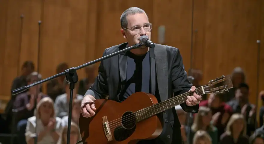 Artysta w okularach gra na gitarze podczas koncertu Męskie Granie. Publiczność w tle.
