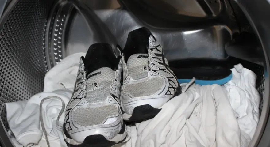 Scarpe da ginnastica pronte per essere lavate in lavatrice, insieme ad alcuni asciugamani bianchi.