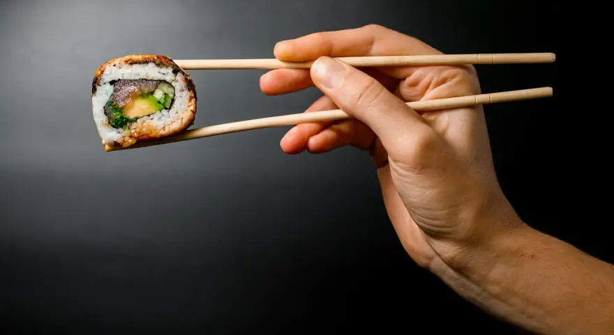 Dłoń trzyma pałeczkami jedno sushi. Zastanawiasz się, ile sushi na osobę będzie idealne na kolację?