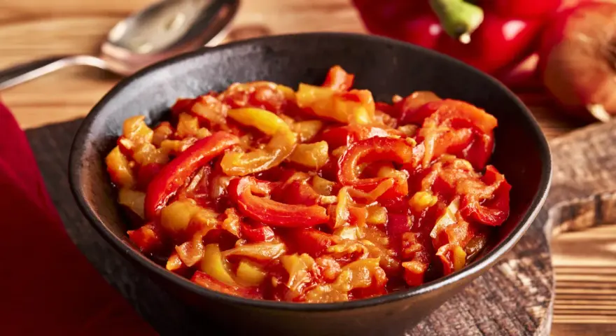 Schmor paprika mit Zwiebeln, ein Gericht, das man gut letscho selber machen kann. Serviert in einer Schüssel auf einem Holztisch.