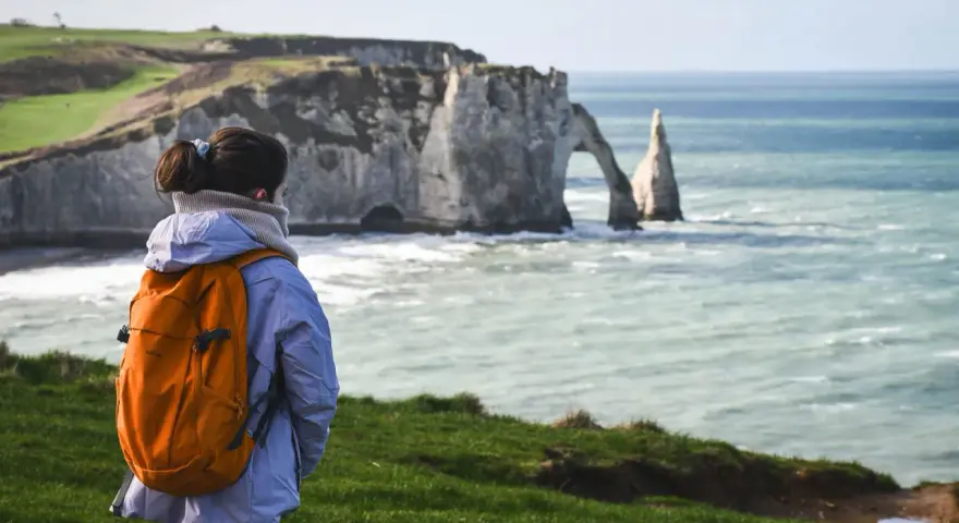 Une randonneuse admire les falaises d'Étretat, un paysage spectaculaire rappelant la beauté sauvage de la baie de Somme.