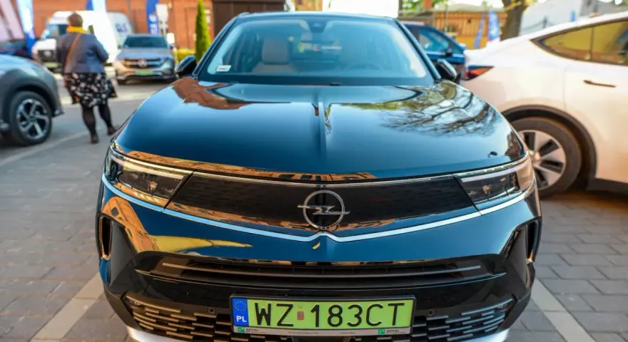 Czarny Opel z zieloną tablicą rejestracyjną WZ 183CT na tle innych samochodów.
