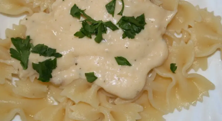Pyszny sos serowy do makaronu farfalle, udekorowany świeżą natką pietruszki. Idealny na szybki obiad.