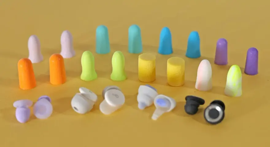 Apprenez comment mettre des bouchons d'oreilles en mousse. Divers bouchons colorés et écouteurs sans fil sont disposés sur fond jaune.