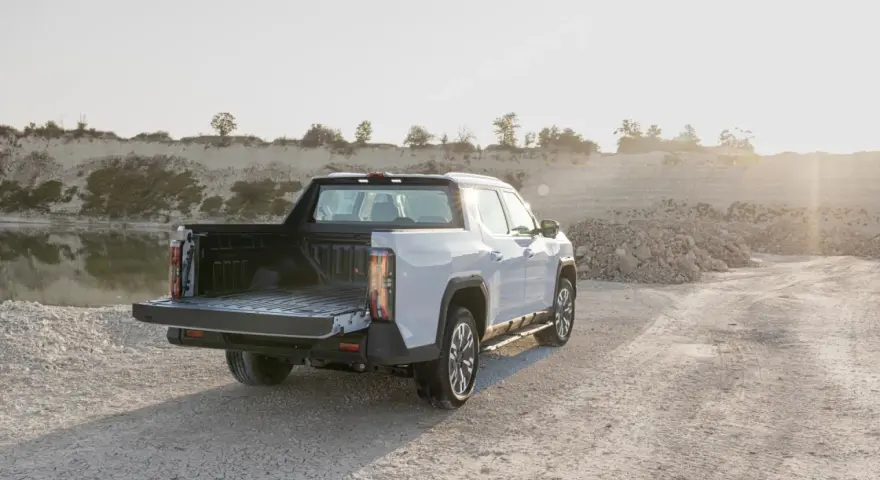 Biały maxus pickup z otwartą paką stoi na żwirowej drodze przy zbiorniku wodnym.