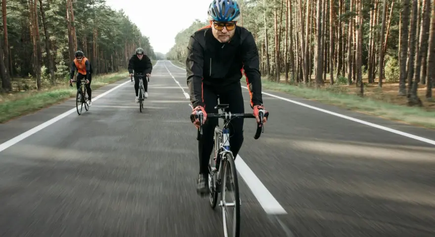 Cyclists on a road through a forest, likely engaged in a VO2 max training program, pushing their limits.