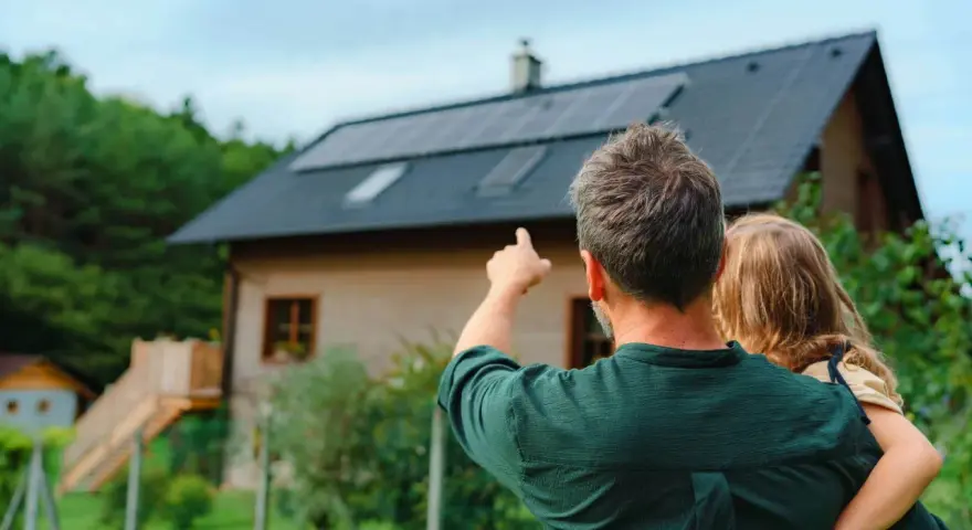 Ojciec z dzieckiem patrzą na dom z panelami fotowoltaicznymi. Zastanawiają się, fotowoltaika 6 kw ile wyprodukuje energii.