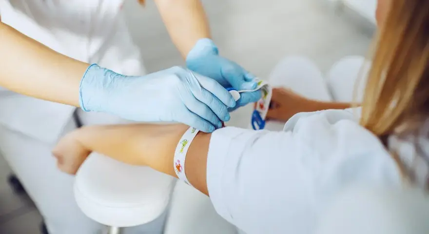 Pielęgniarka w rękawiczkach zakłada opaskę uciskową przed pobraniem krwi. Dowiedz się, gdzie zrobić badania krwi na NFZ.