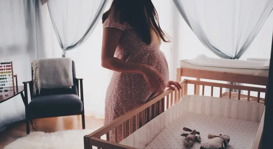 En gravid kvinna vid en spjälsäng, med en känsla av oro som kan associeras med gravid depression.