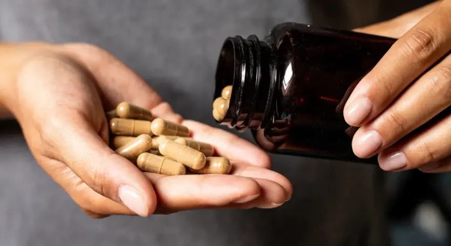 Hände schütten Kapseln aus einer braunen Flasche. Die Kapseln liegen in der Handfläche, bereit zur Einnahme. Möglicherweise zur Unterstützung der chrom wirkung.