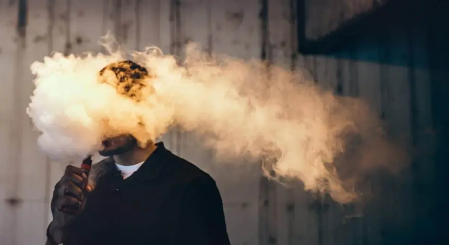 Hombre exhalando una gran nube de humo vaper, que envuelve su cabeza.