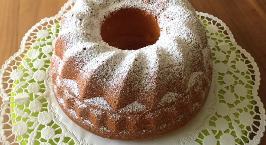 Ein goldbrauner Quark Gugelhupf, bestäubt mit Puderzucker, auf einer zarten Spitzendeckchen.