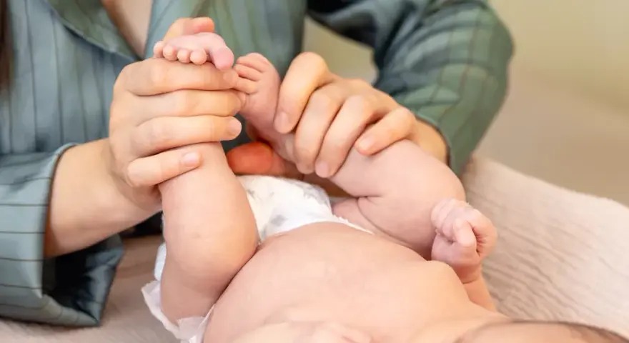 Mani che massaggiano le gambine di un neonato, un gesto d'amore per capire se il neonato ha le coliche e alleviare il suo disagio.