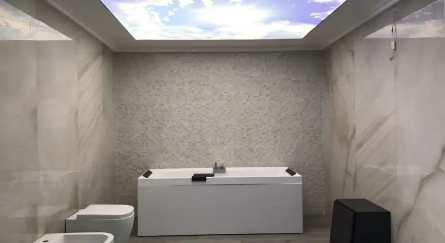 Bagno moderno con vasca, bidet e WC. Il soffitto in cartongesso riproduce un cielo azzurro con nuvole, creando un'atmosfera rilassante.
