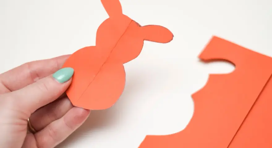 En hand håller en orange pappersfigur av en påskhare.