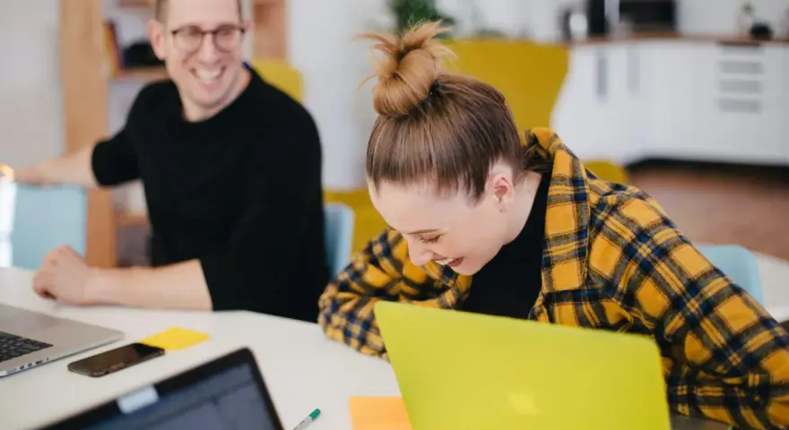 Zwei lachende Kollegen am Schreibtisch mit Laptops. Ein bezahltes Auslandspraktikum kann so Spaß machen!