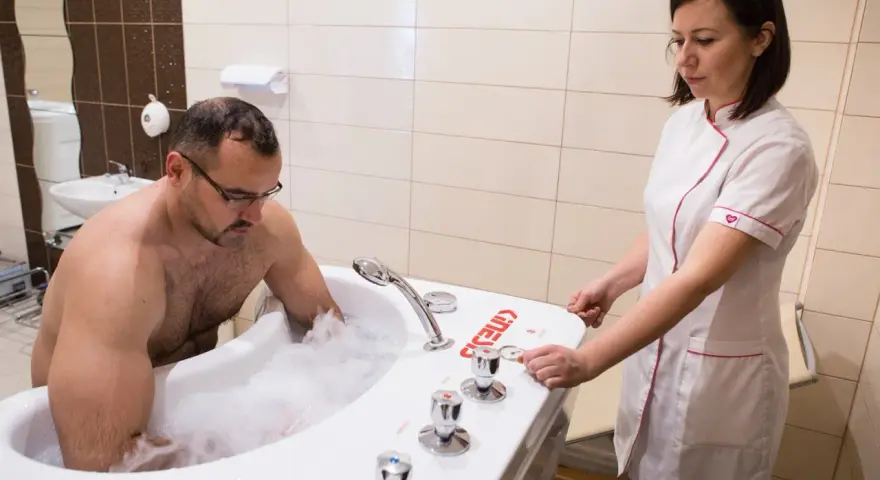 Mężczyzna w wannie z pianą, terapeuta przygotowuje masaż wirowy kończyn dolnych.