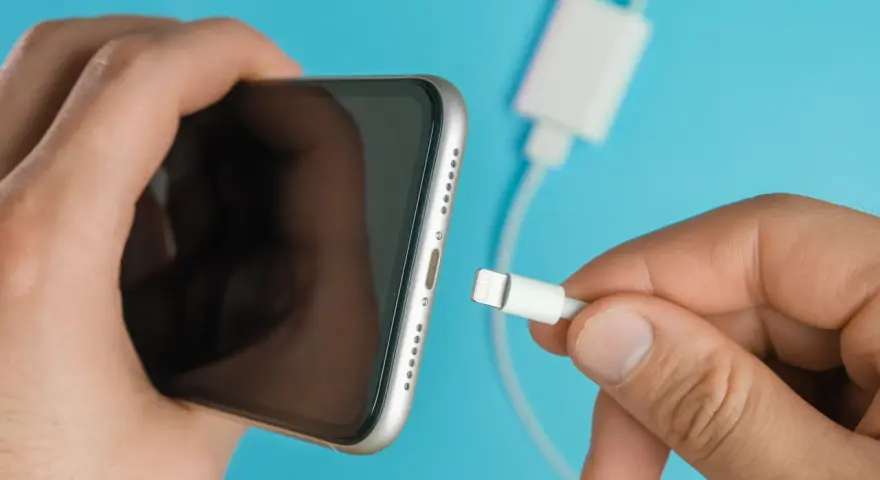 En hand håller en iPhone och en laddkabel. Var försiktig med vatten i ladduttaget på din iPhone.
