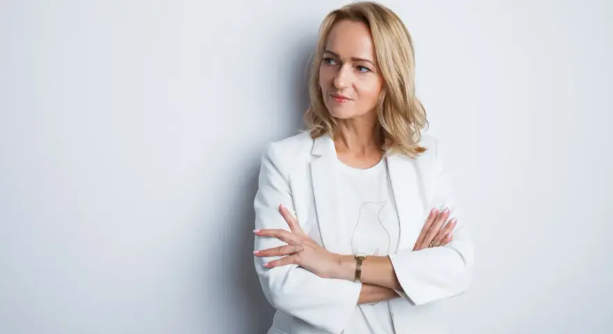 Elegancka kobieta w białej marynarce, z rękami skrzyżowanymi na piersi. Idealne zdjęcie do CV, podkreślające profesjonalizm i pewność siebie.