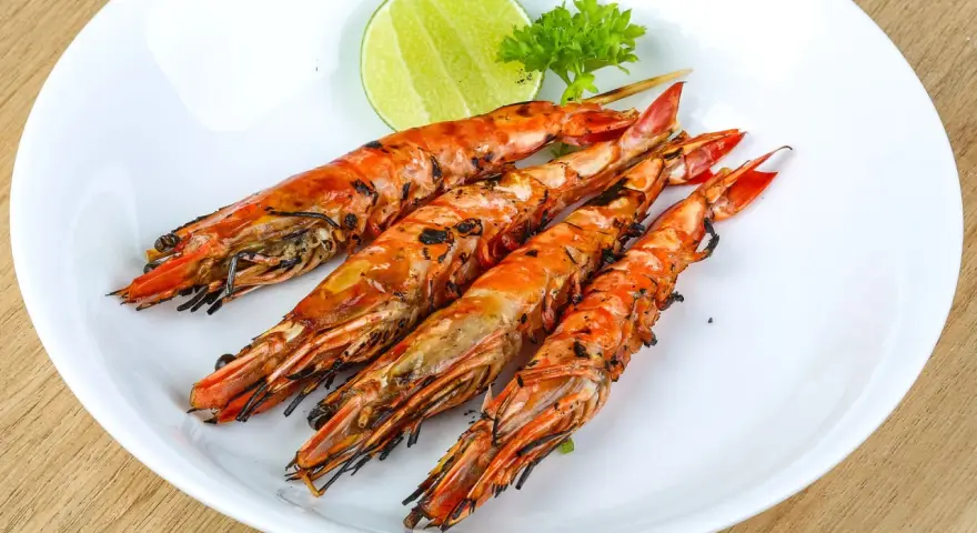 Cuatro langostinos a la plancha, dorados y jugosos, servidos en plato blanco con rodaja de limón y perejil.