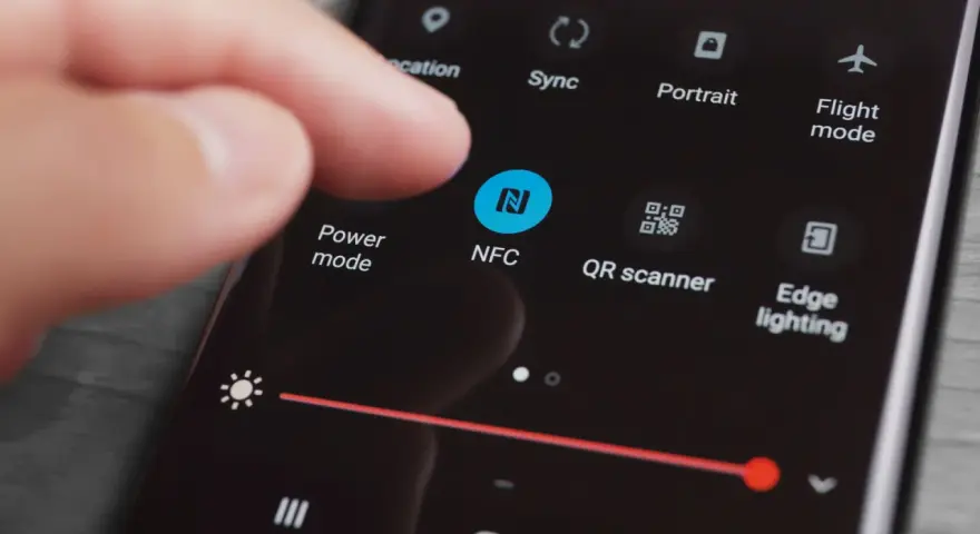 En finger pekar på NFC-ikonen på en mobilskärm. Snabbinställningar visas, inklusive "Power mode" och "QR scanner".