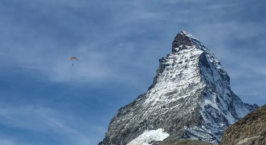 Widok na ośnieżony szczyt Matterhornu, z paralotnią szybującą na błękitnym niebie. To jak wejście na Mont Blanc dla odważnych.