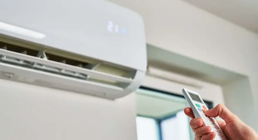 Mano operando el control remoto de un aire acondicionado, indicando la temperatura de 21 grados. Es hora del mantenimiento.