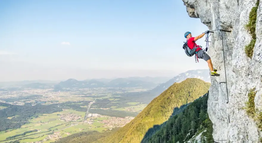 Ein Mann klettert gesichert an einem Stahlseil einen Felsgrat entlang. Ein Abenteuer auf einem der vielen Klettersteige Deutschlands.