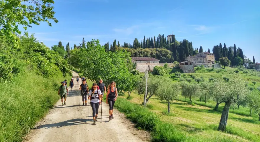 Gruppo di escursionisti su sentiero sterrato, con case coloniche e cipressi sullo sfondo. La Via degli Dei, nonostante la bellezza, presenta una certa difficoltà.