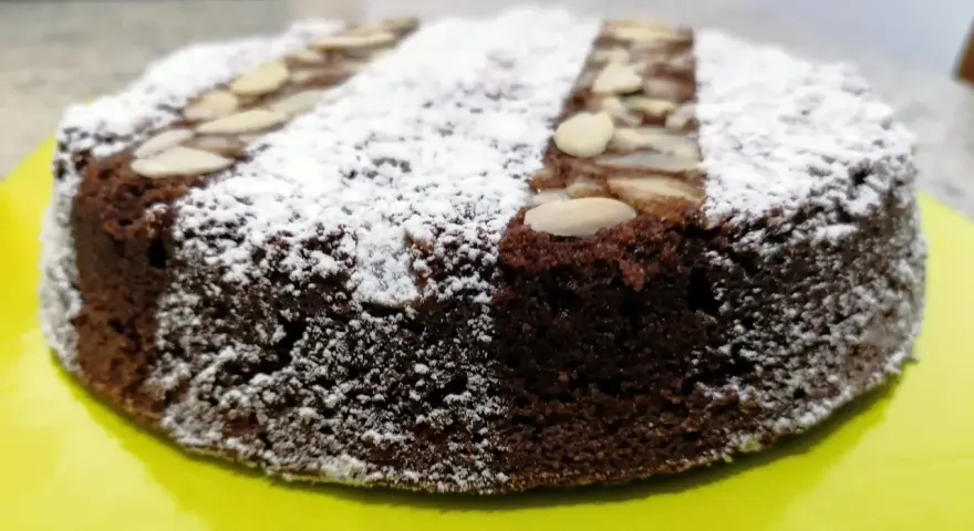 Torta caprese ricetta originale napoletana, soffice e scura, cosparsa di zucchero a velo e mandorle a lamelle.