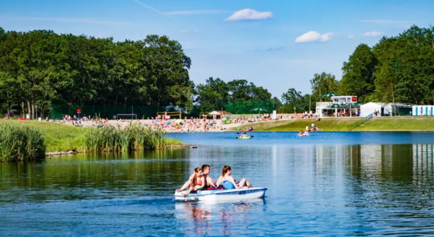 Rodzina na rowerku wodnym na jeziorze, plaża pełna ludzi, las i budynki w tle. Idealne miejsce gdzie nad wodę Dolny Śląsk.