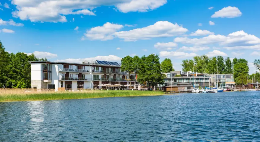 Nowoczesny Tiffi Hotel Olsztyn nad jeziorem, z łodziami przy pomoście i zielenią.