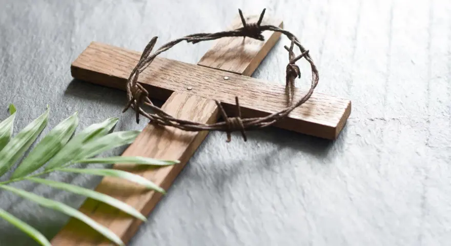 Holzkreuz mit Dornenkrone und Palmblatt. Christen fasten Regeln, um sich auf Ostern vorzubereiten.