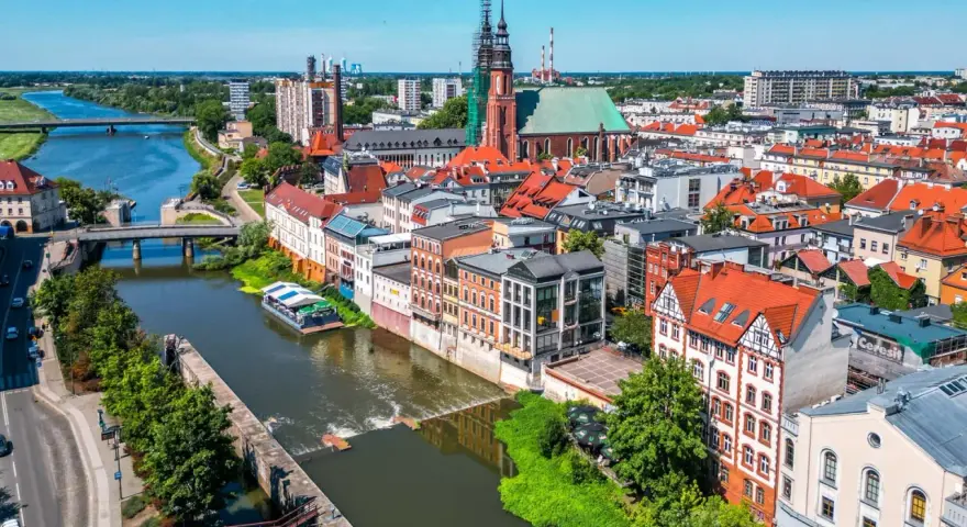 Widok na Odrę i zabytkowe centrum Opola. Rzeka, mosty, kościół i kamienice tworzą malowniczy krajobraz, idealny do odkrywania opolskich atrakcji.