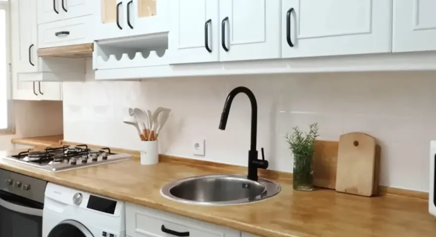 Cocina renovada: gabinetes blancos, encimera de madera y grifo negro. ¡Un ejemplo de cómo pintar muebles de melamina para darles nueva vida!