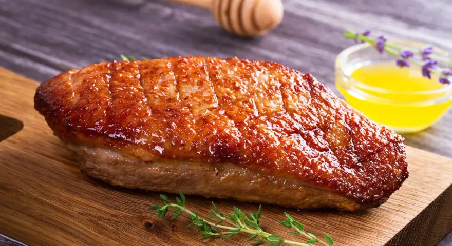 Un magret de canard au barbecue, la peau dorée et croustillante, prêt à être dégusté avec une touche de miel et de thym.