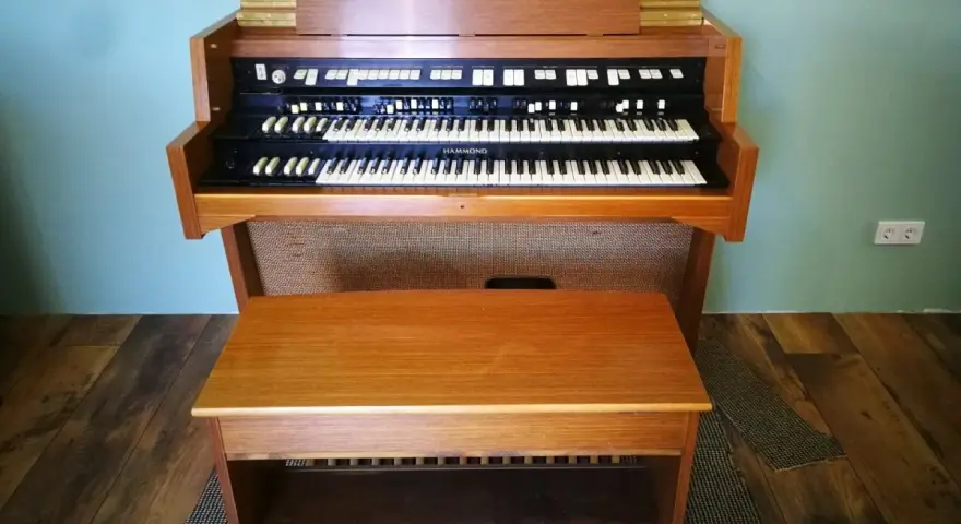 Ein schönes Hammond-Musikinstrument mit zwei Manualen und einer Holzbank davor.