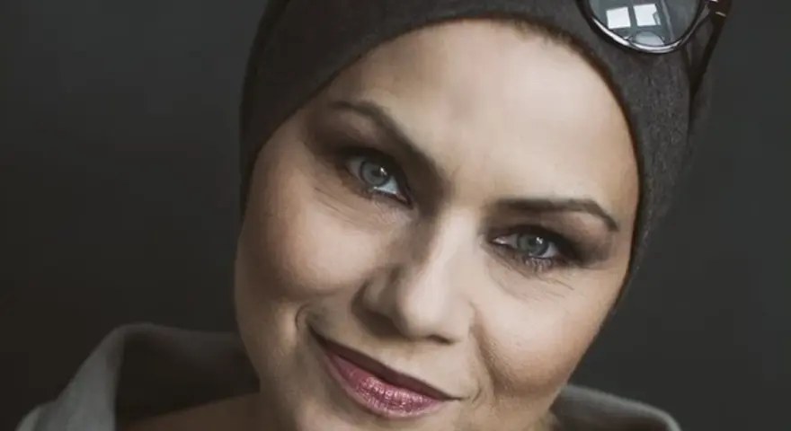 Sylwia Janowicz-Dobrowolska w szarej opasce i okularach na głowie, z wyrazistym makijażem oczu i błyszczącymi ustami.