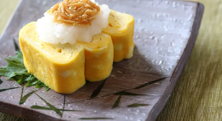 Roladki tamago z tartą rzodkwią i grzybami enoki na talerzu z motywem bambusa.